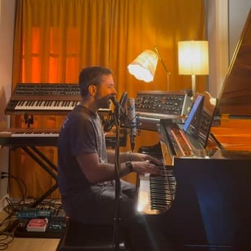 Dan at the piano, singing into a mic with the Prophet-5 and Model D visible on stands behind